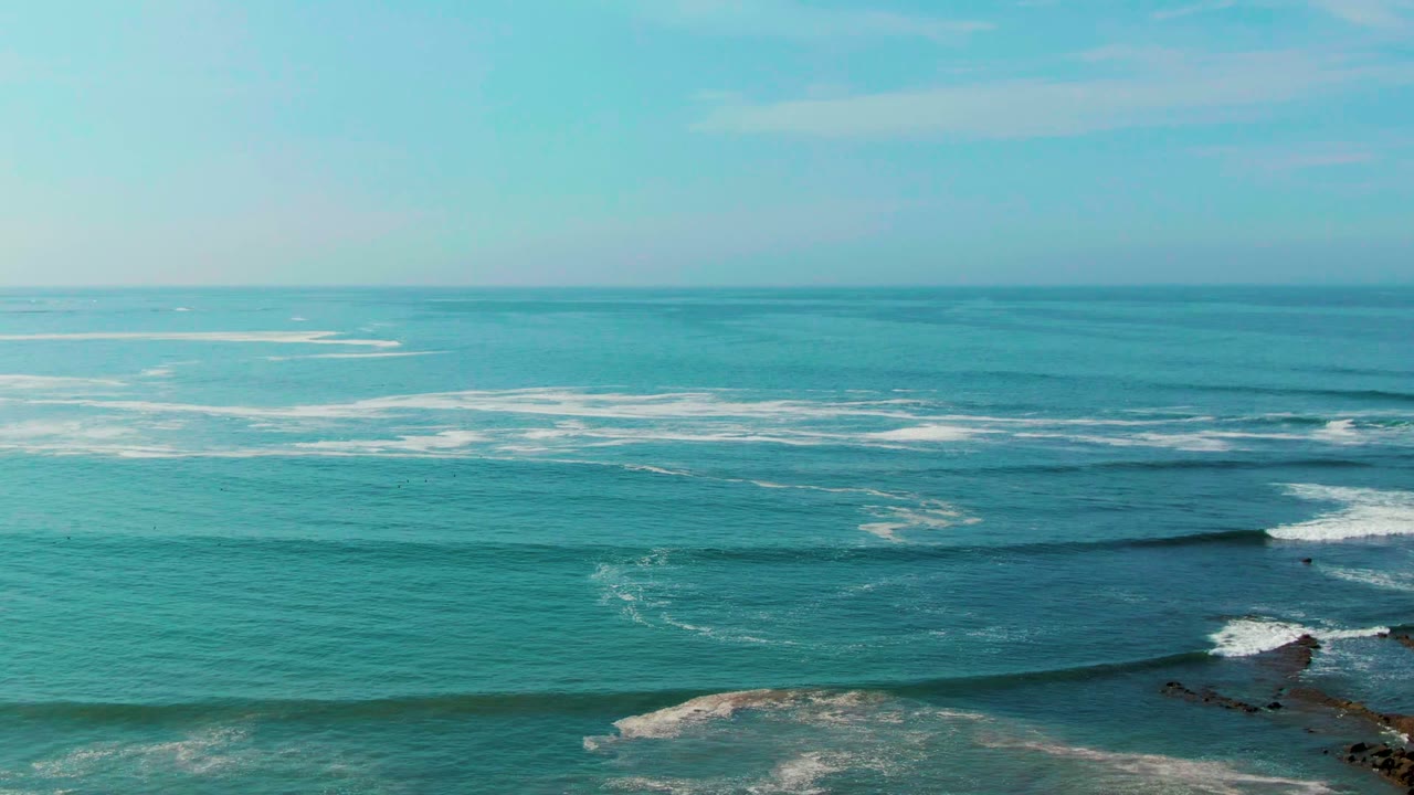 Blue-green ocean with breaking waves and a small rocky point at lower right.