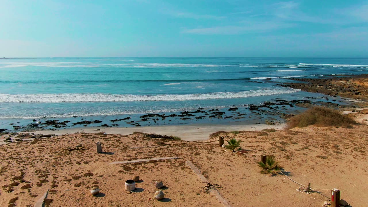Empty beach with rocks, bucket, surf line, and blue ocean.