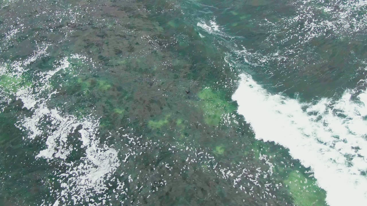 Top-down ocean view at La Bocana, Baja California Sur, with a larger white surf patch entering over blue-green water and no visible people.