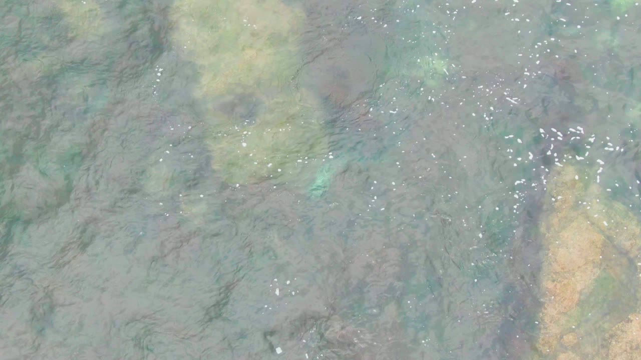 Clear water in La Bocana, Baja California Sur, ripples over pale submerged rocks with scattered white bubbles and no visible people.