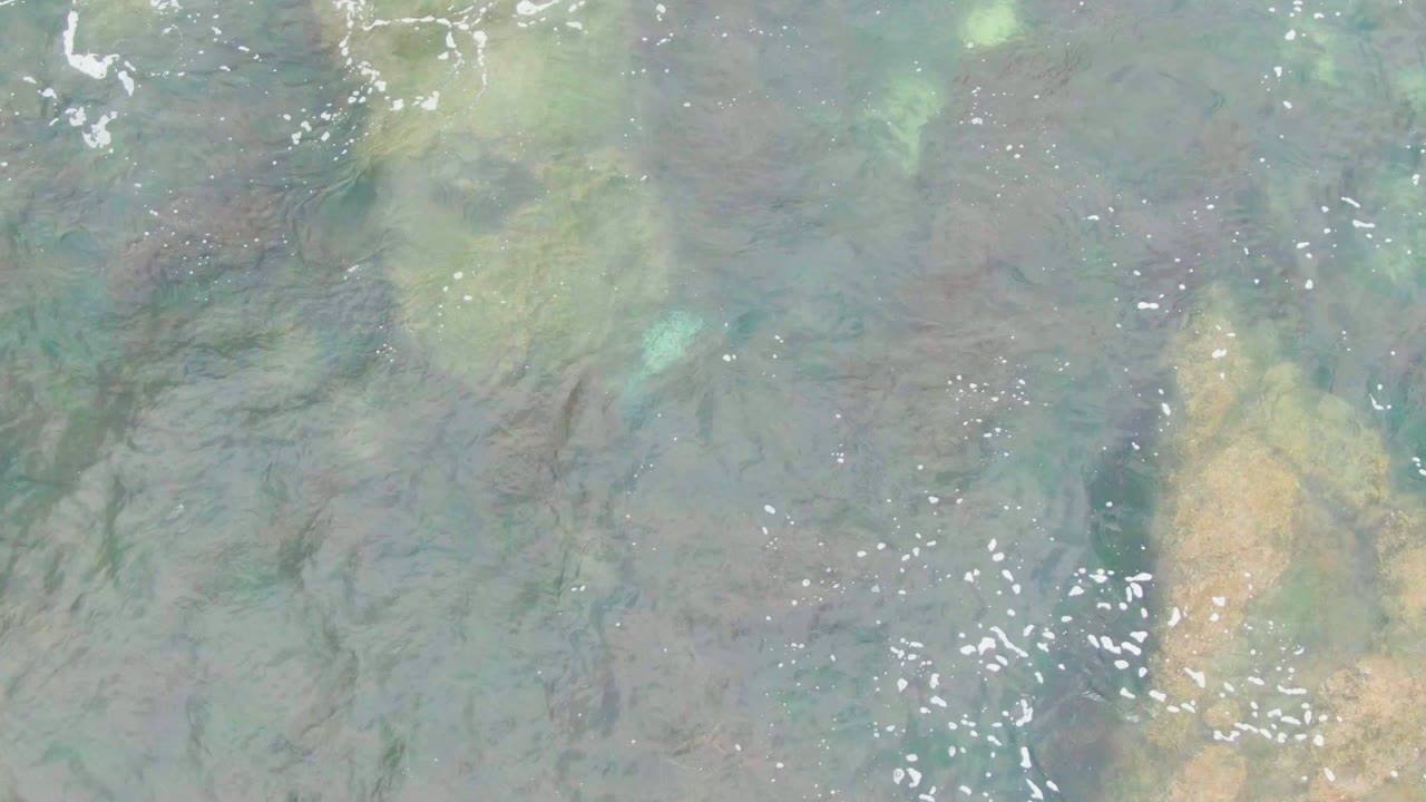 At two seconds, clear water in La Bocana passes over a vertical tan seabed patch, darker rock lines, and small white foam flecks with no visible people.