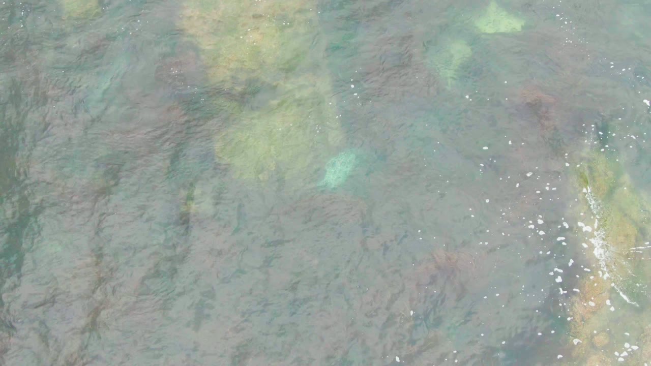 Overhead La Bocana water detail with green and tan seabed shapes under blue-green ripples, small surface sparkles, and no visible people.