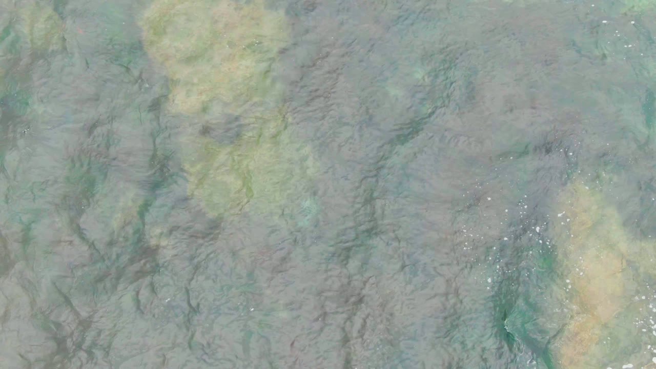 Top-down view of clear shallow water in La Bocana, Baja California Sur, with dark seabed lines, pale tan underwater patches, and no visible people.