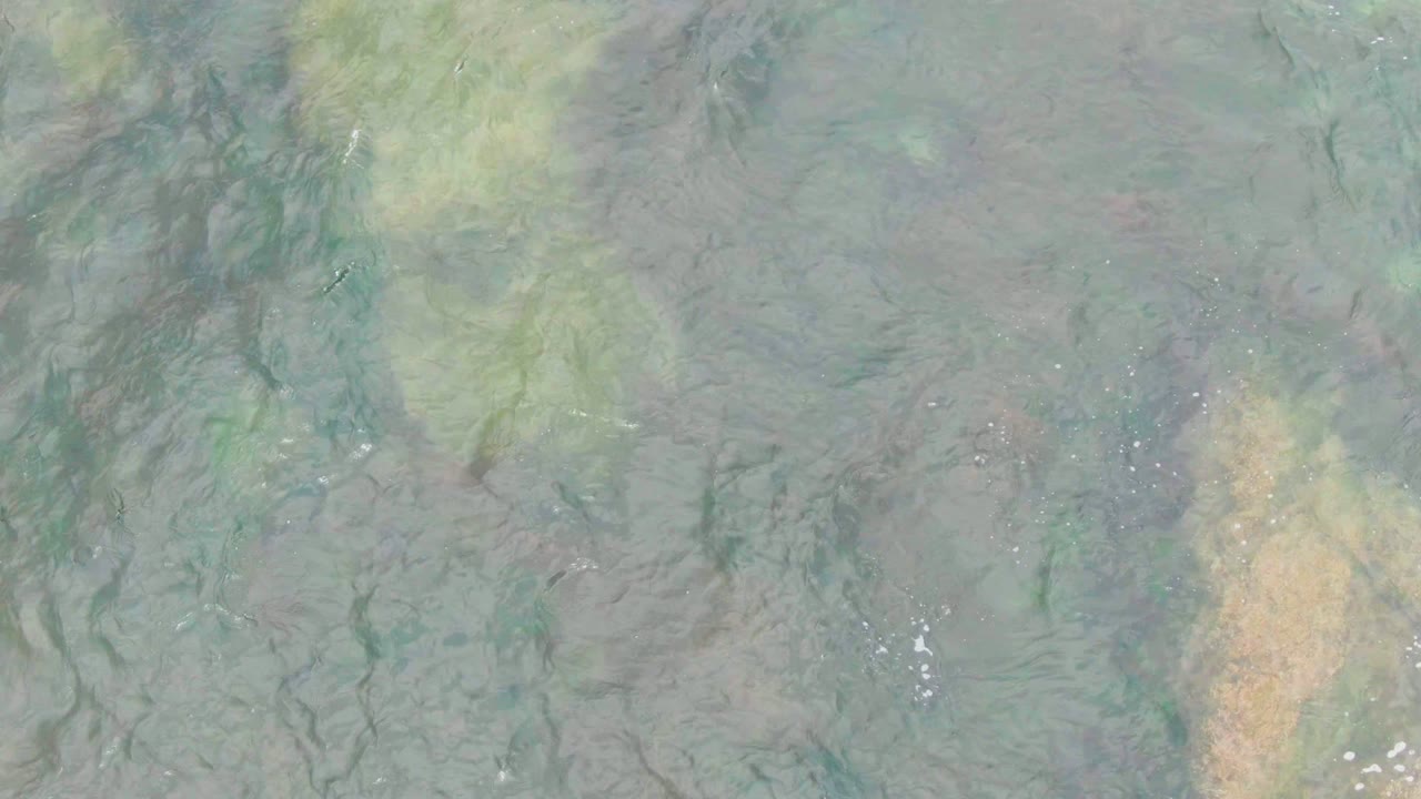The aerial view over La Bocana water shows a pale tan seabed patch near the upper area, darker rock lines below it, and no visible people.
