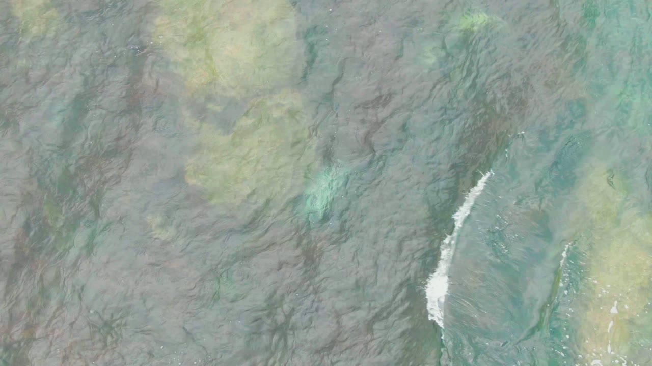 White foam crossing shallow green water from above