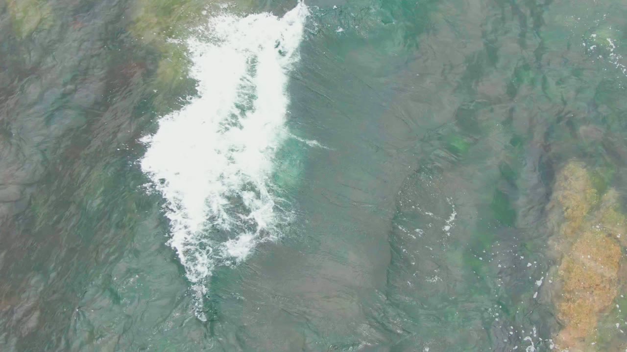 A bright foamy wave line breaks across green shallow water at La Bocana, Baja California Sur, while darker underwater textures remain visible and no people appear.