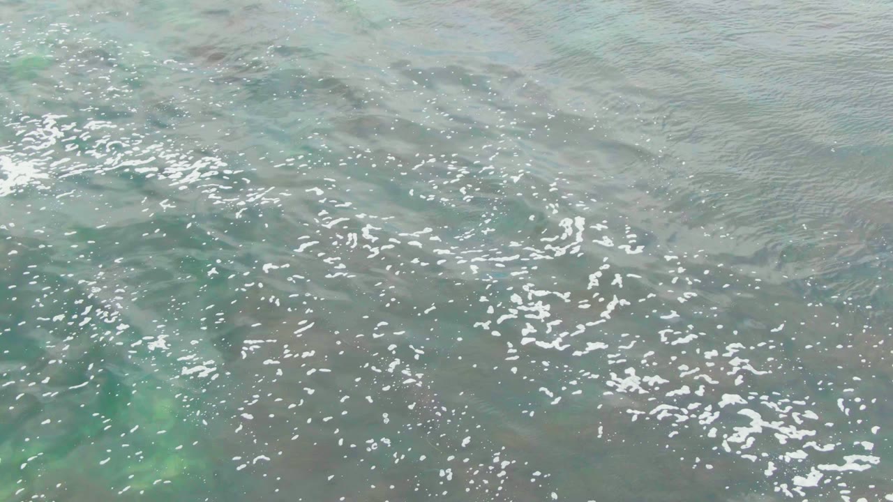 Turquoise ocean ripples with bright foam patches