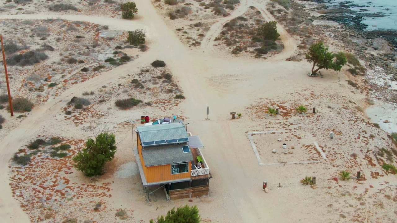 Drone view of a solar-roof house beside dirt roads in arid terrain.
