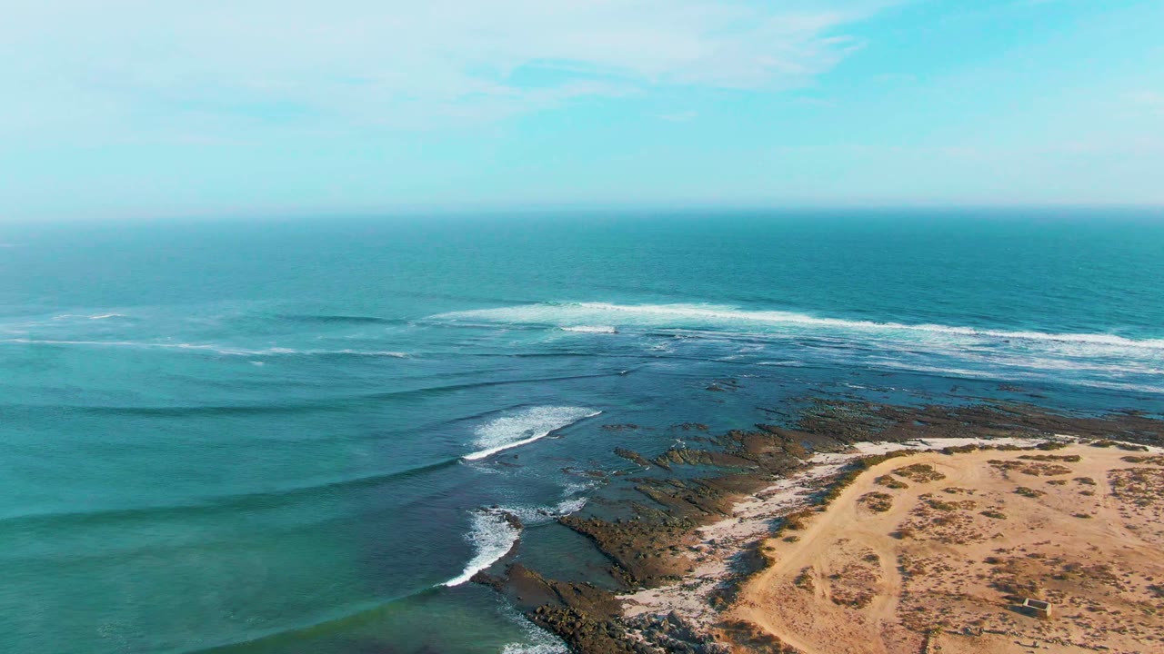 La Bocana aerial frame with long ocean swell bands crossing teal water, white foam over the reef, sandy shoreline in the lower right corner, and no visible people.
