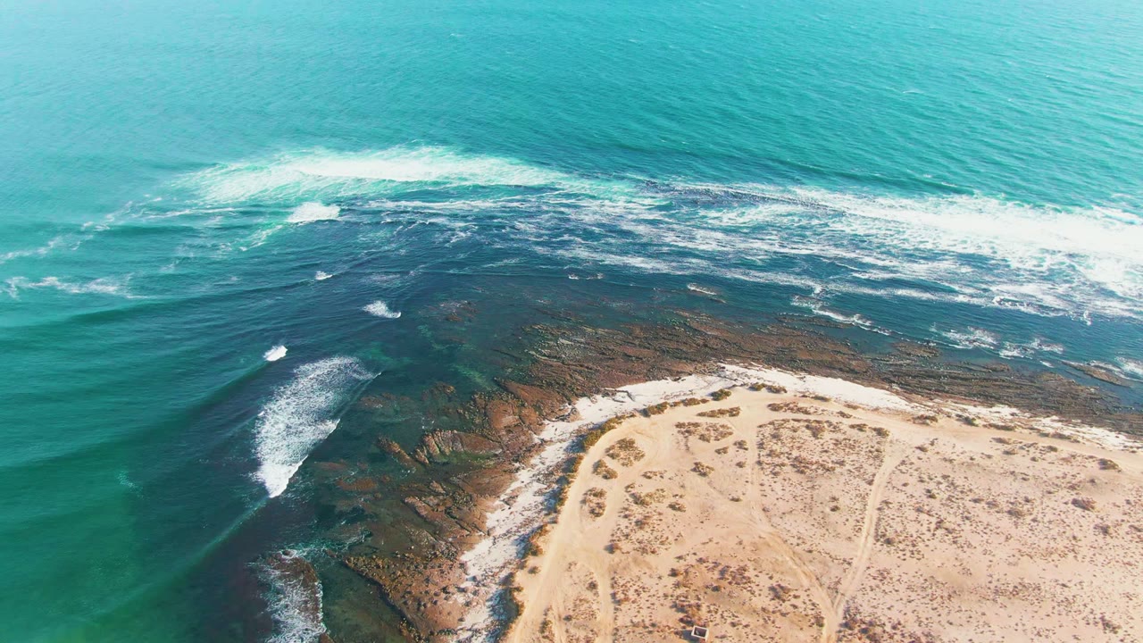 White waves spread across a rocky reef with pale sand below.