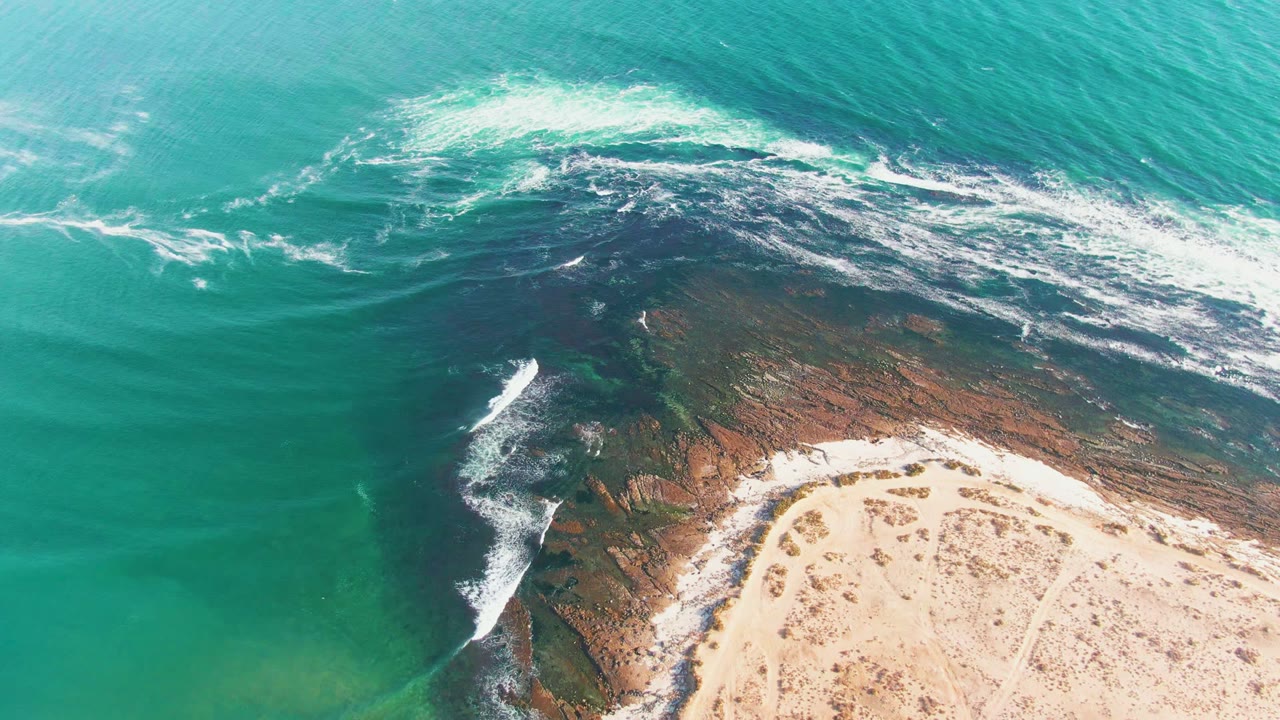White wave foam curls along a rocky reef near a sandy beach.