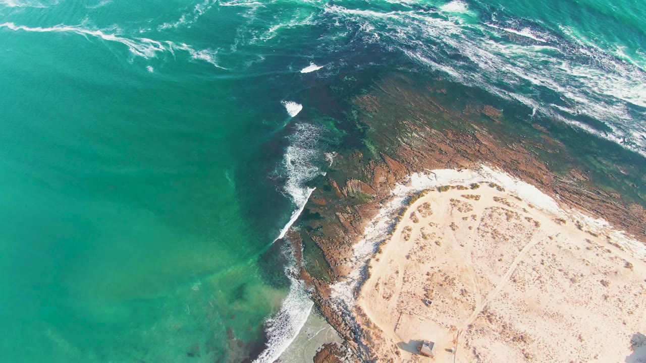 Drone view of waves breaking along a rocky shoreline beside sand