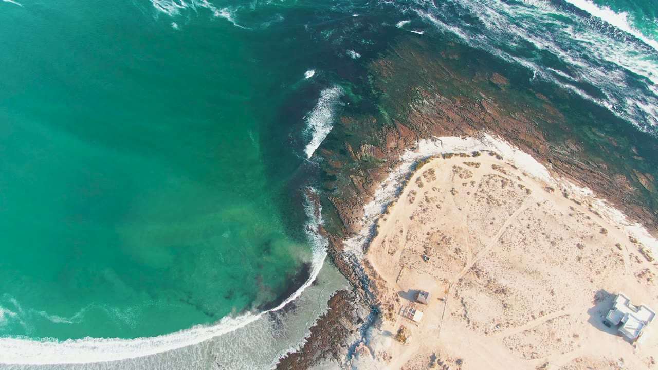 Turquoise water and white foam curl along a sandy beach and rocky shelf.