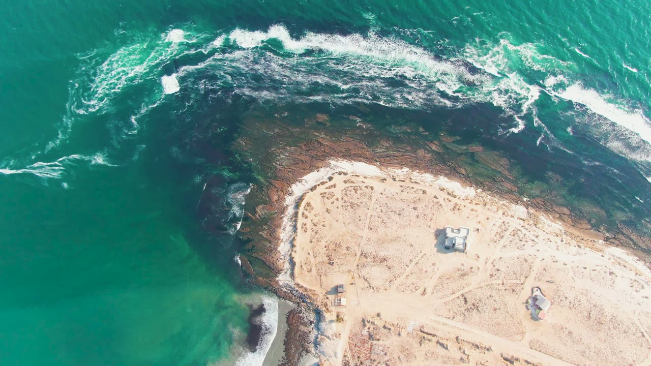 Surf line beside pale sand and dark coastal rocks