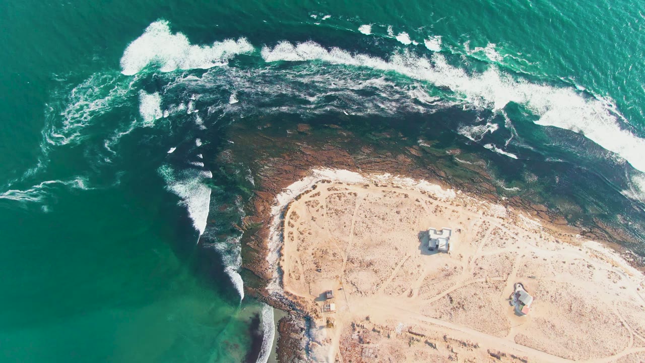 White foam breaks over dark shallows beside a sandy point