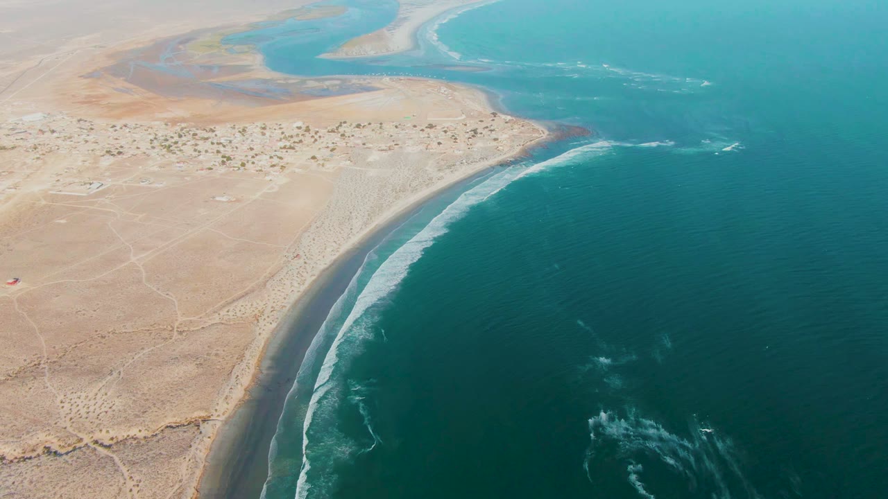 Drone-height frame of La Bocana coastline showing a desert point, surf tracing the beach edge, turquoise shallows in the distance, and no visible people.