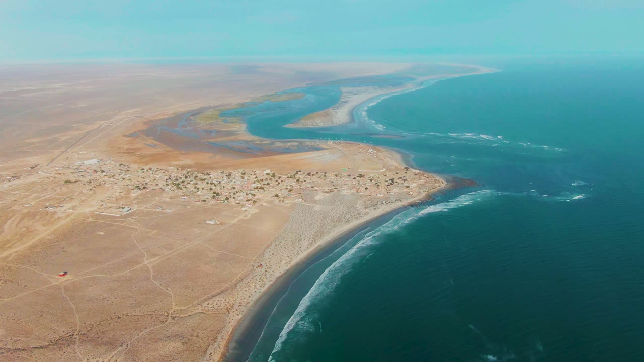Aerial view of La Bocana desert village beside a curved beach, lagoon, and blue ocean.