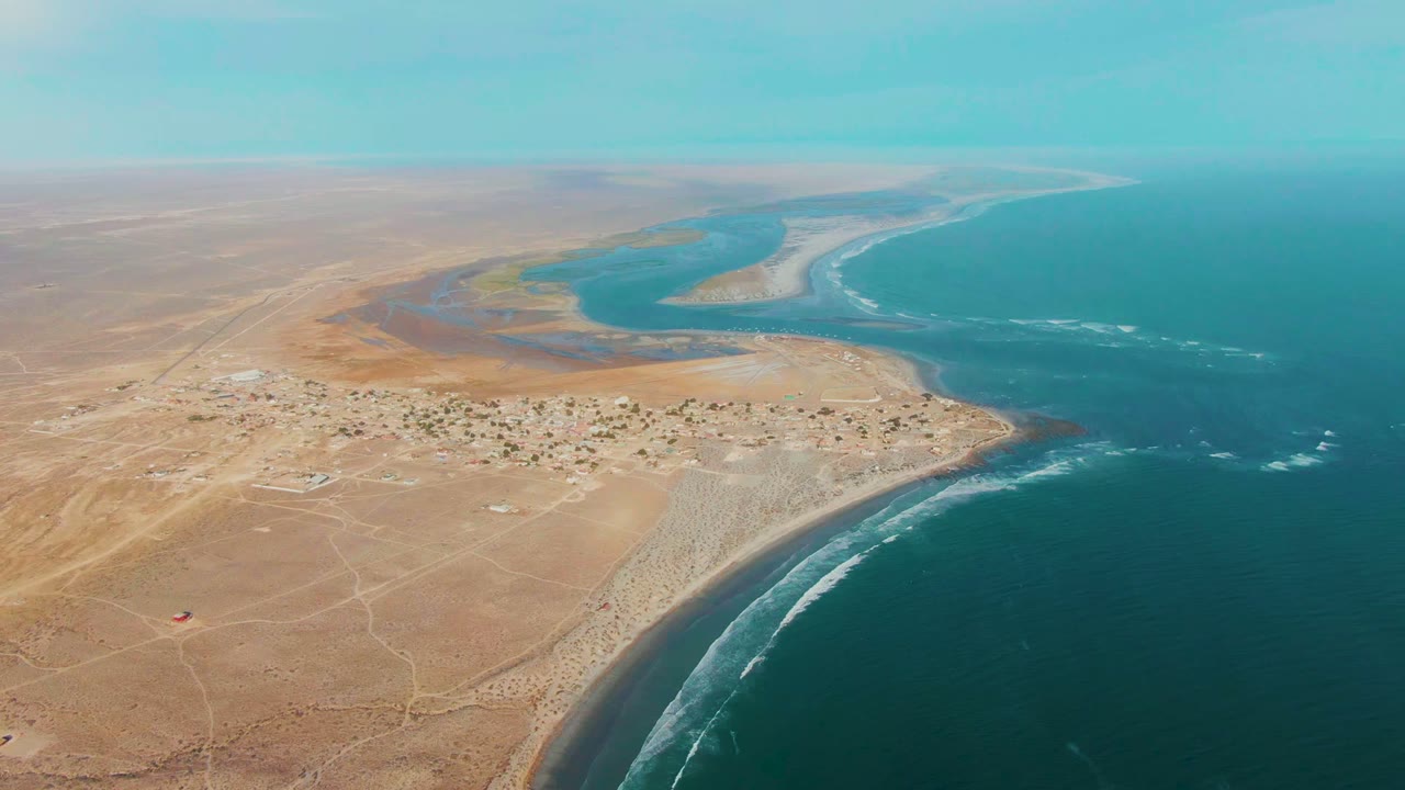 Coastal desert town with surf and inlet seen from above