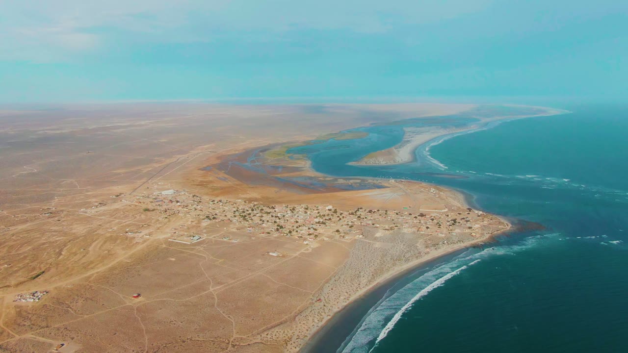 A La Bocana aerial view with scattered buildings on the desert edge, white wave bands along the shore, blue-green lagoon water, and no visible people.