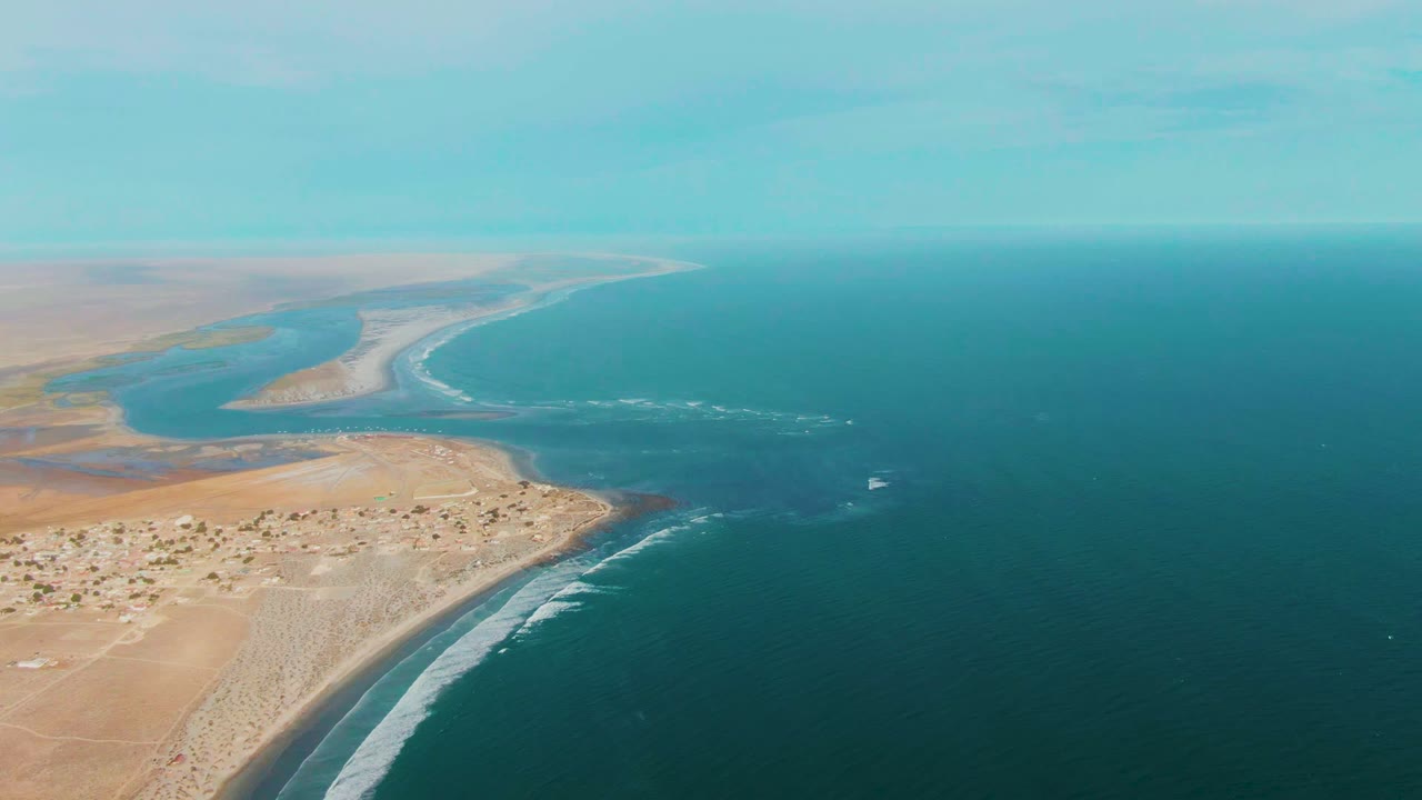 Desert shoreline with river channel, coastal buildings, surf, and blue ocean