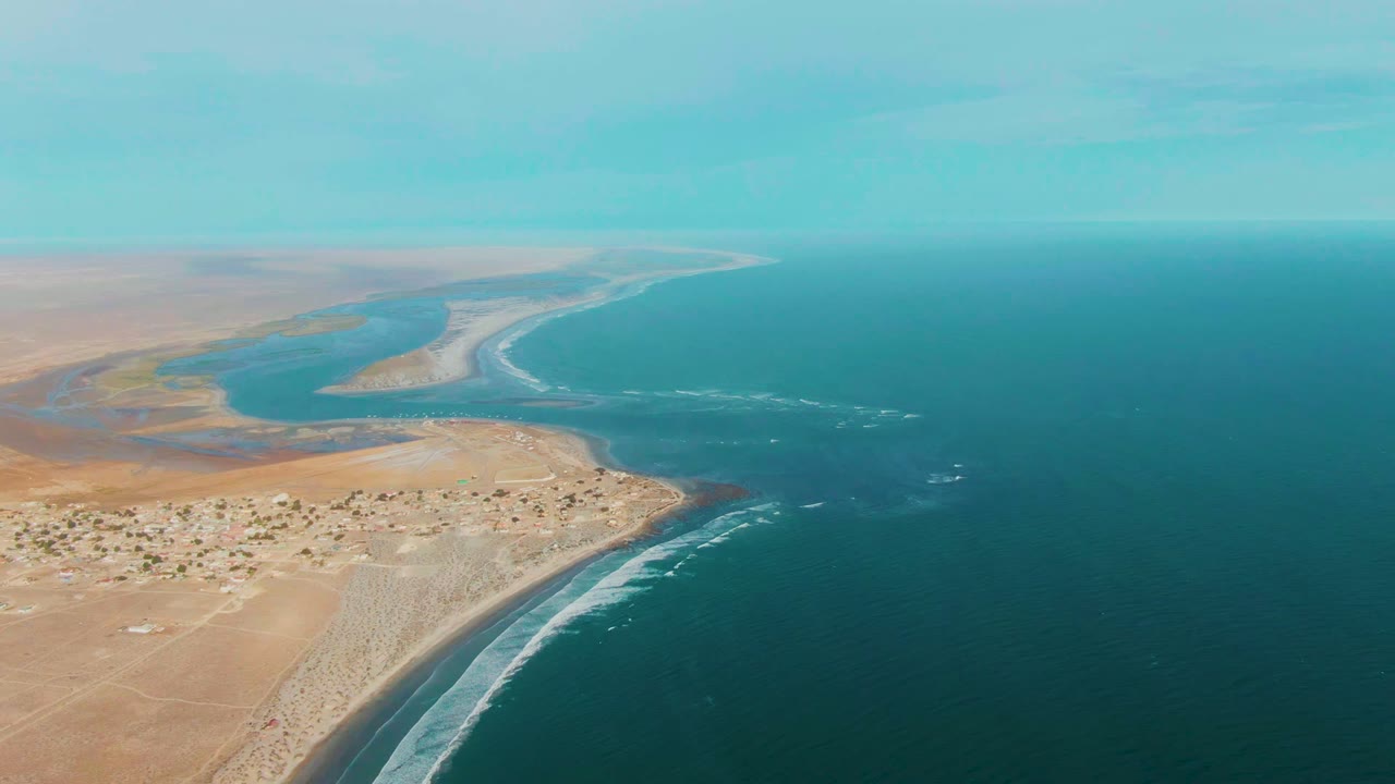Aerial coastline with river channel, surf lines, sand, and ocean.
