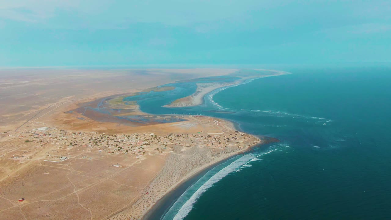 High aerial view of a desert lagoon curving toward ocean waves.
