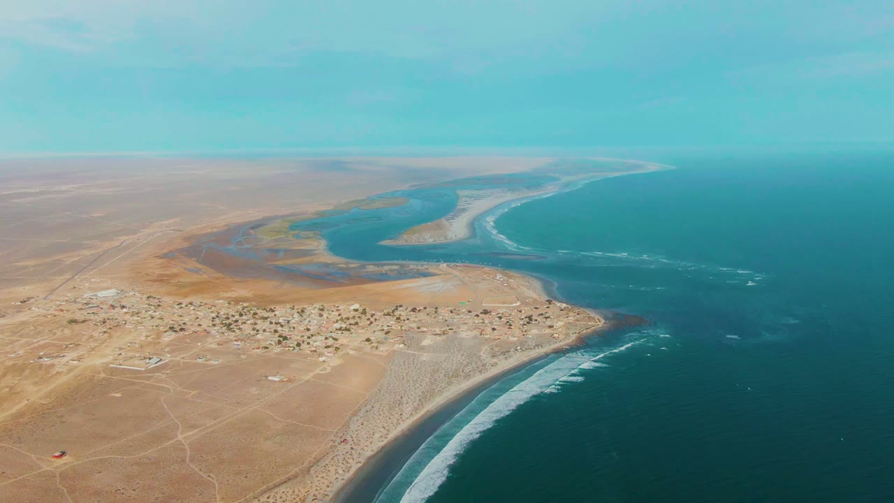 High drone frame over La Bocana showing turquoise lagoon pools, pale sandbars, dark blue ocean, tan arid land, and no visible people.