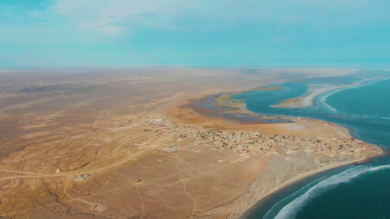 Small coastal settlement on sandy desert land beside surf