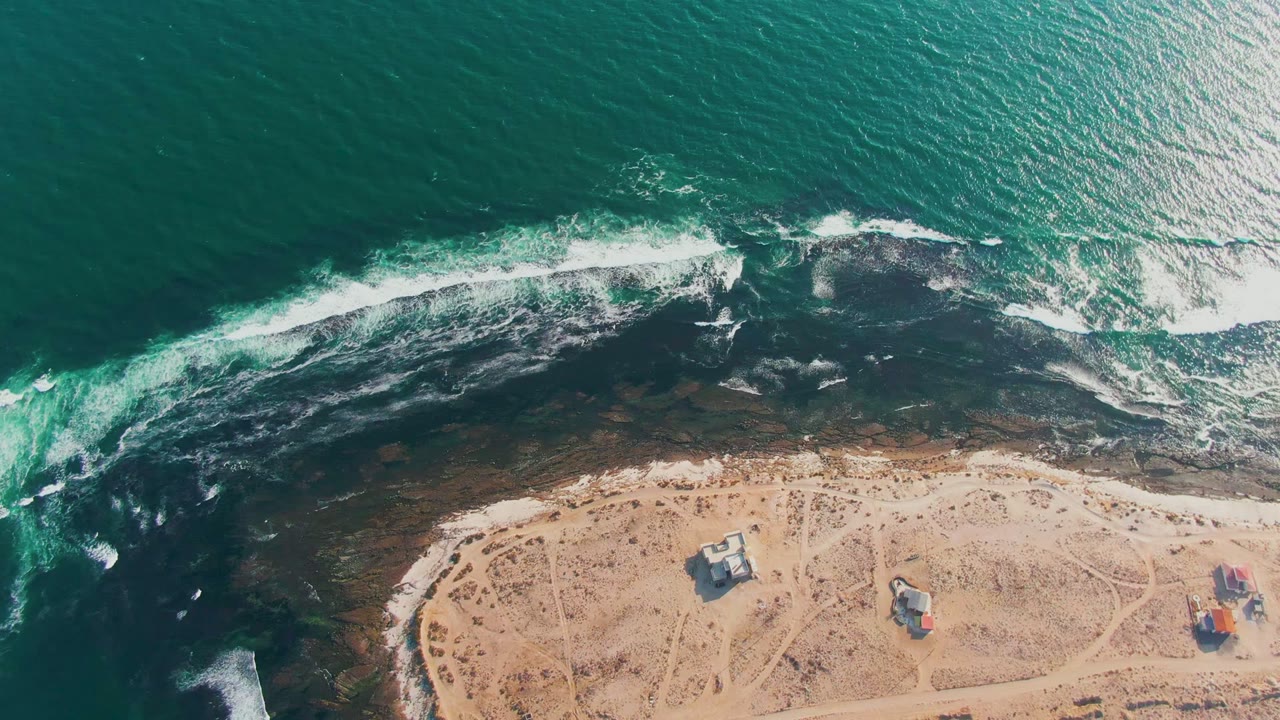 Aerial coastline with white foam curling over rocks and sand