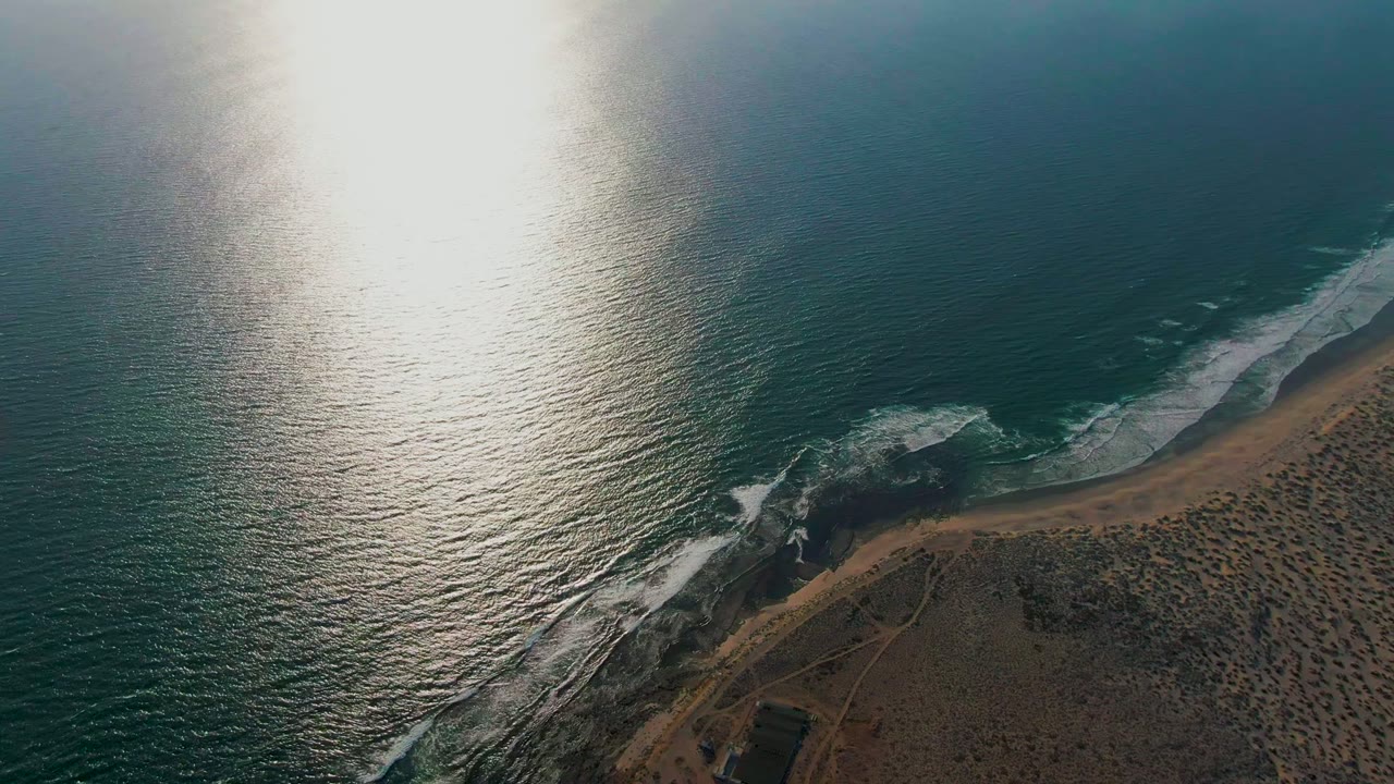 Sun glare over ocean water with foam washing along a curved beach.