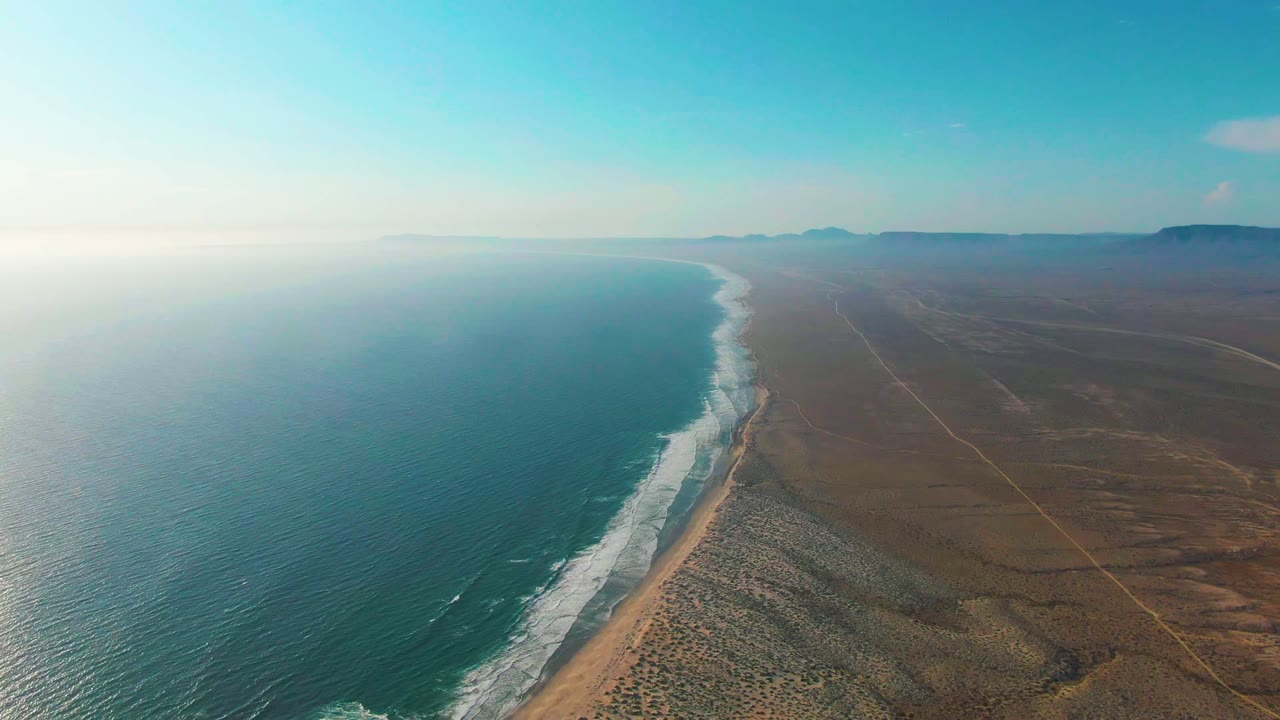 Wide drone view of waves curling along a remote desert beach.