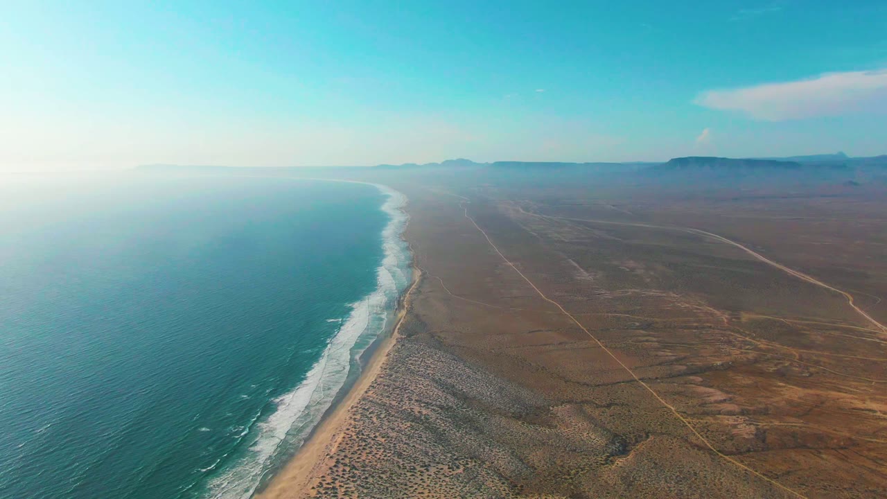 Wide aerial coastline with waves and open desert inland.