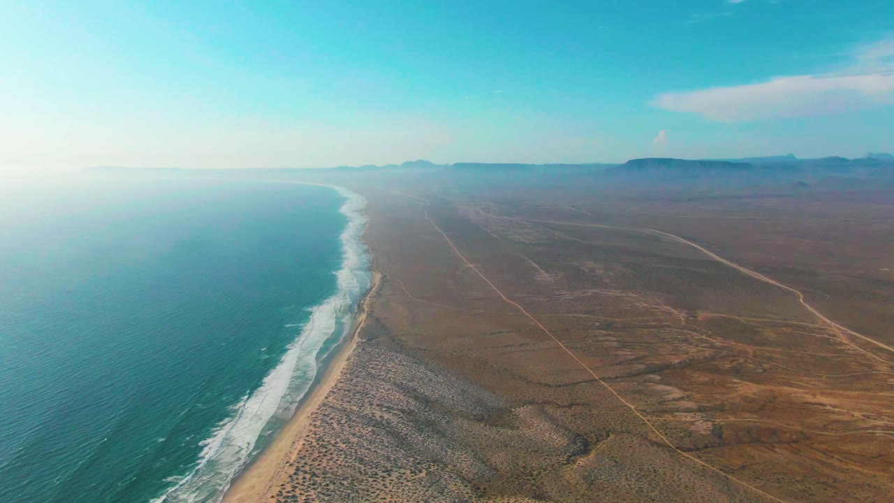 Wide aerial coastline with waves and arid inland plain
