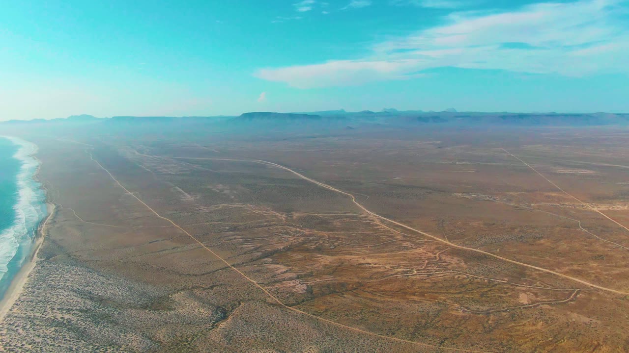 Drone view of desert coastline with roads and distant mountains