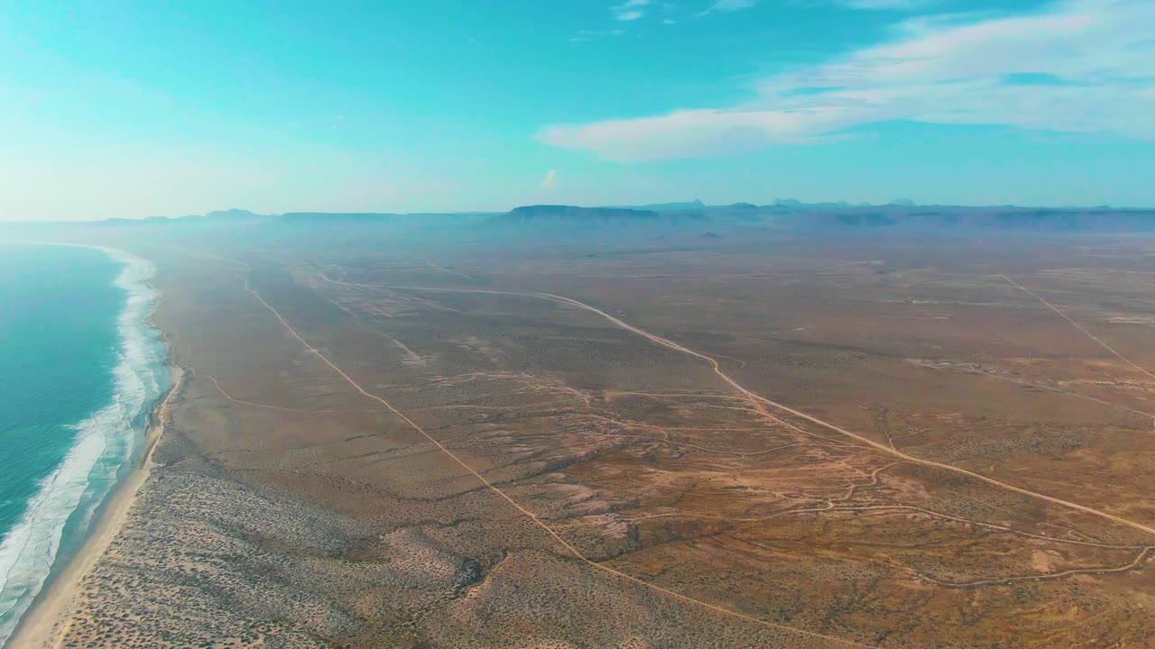 Wide drone view of beach, surf, and inland desert roads.