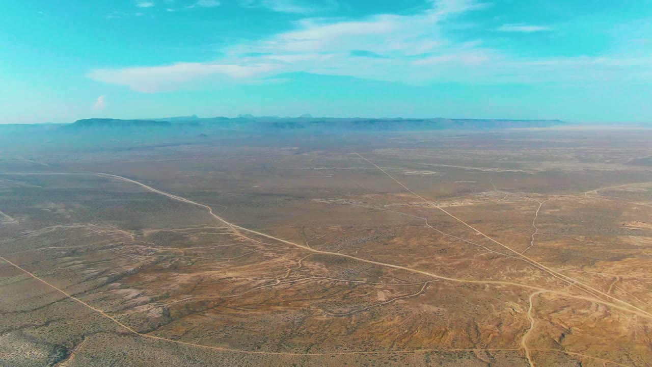 Wide arid terrain with intersecting dirt tracks under blue sky
