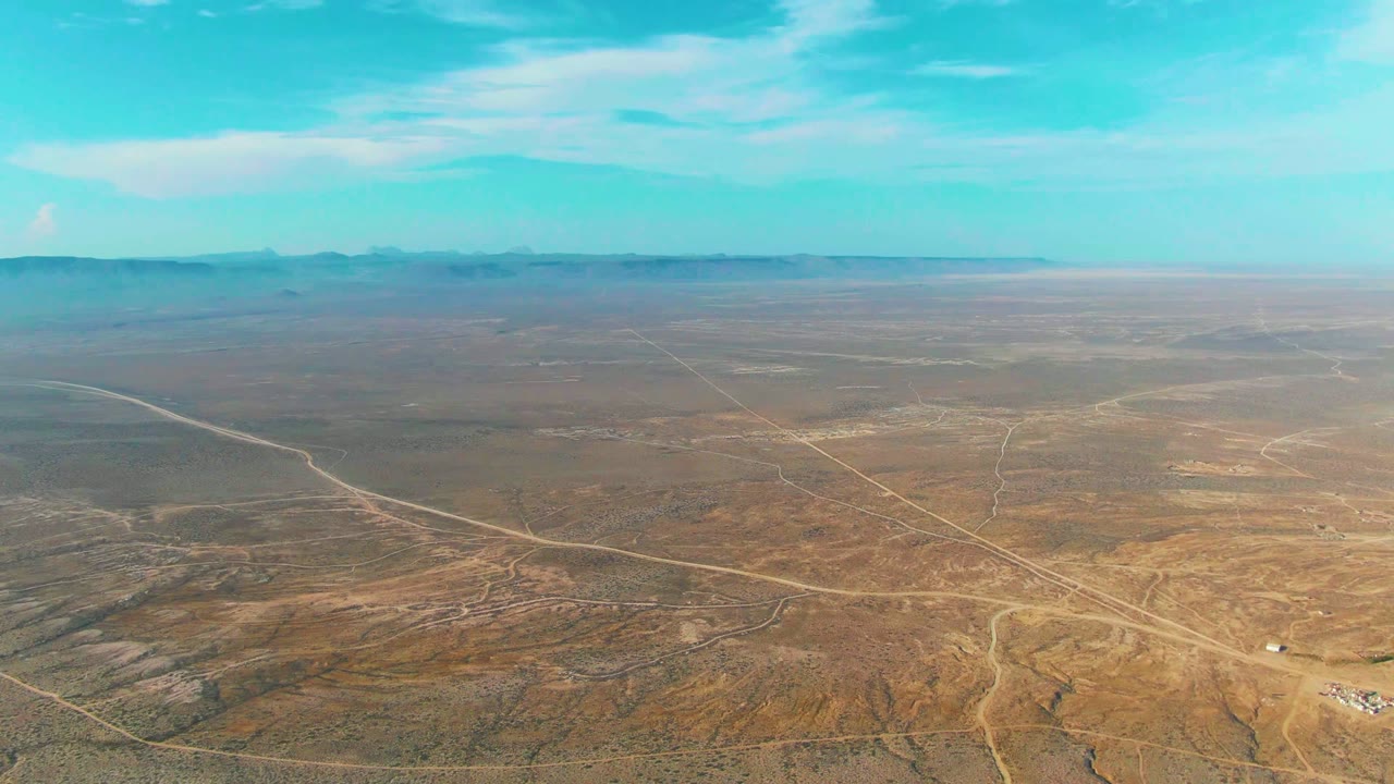 La Bocana aerial desert view with a pale road sweeping in from the left, faint tracks across the midground, distant mountains, and no visible people.