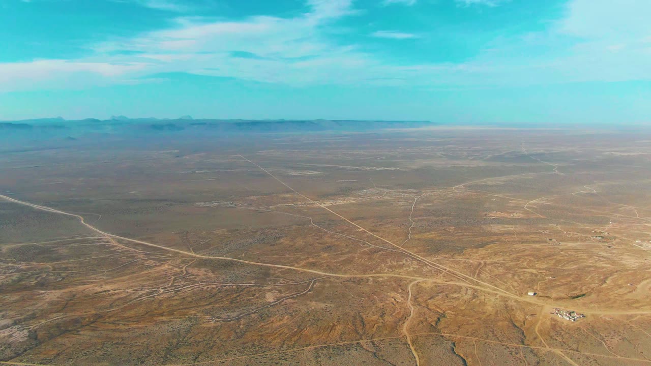 A second aerial view of La Bocana, Baja California Sur shows the road grid spread across dry terrain, with mountains softened by haze and no visible people.