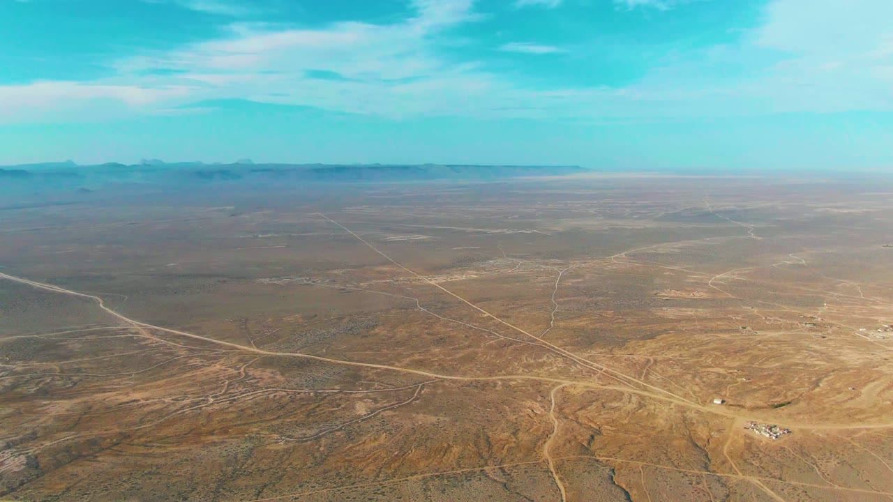 Aerial frame over La Bocana, Baja California Sur with multiple dirt tracks converging across brown desert, a low mountain line in the background, and no visible people.