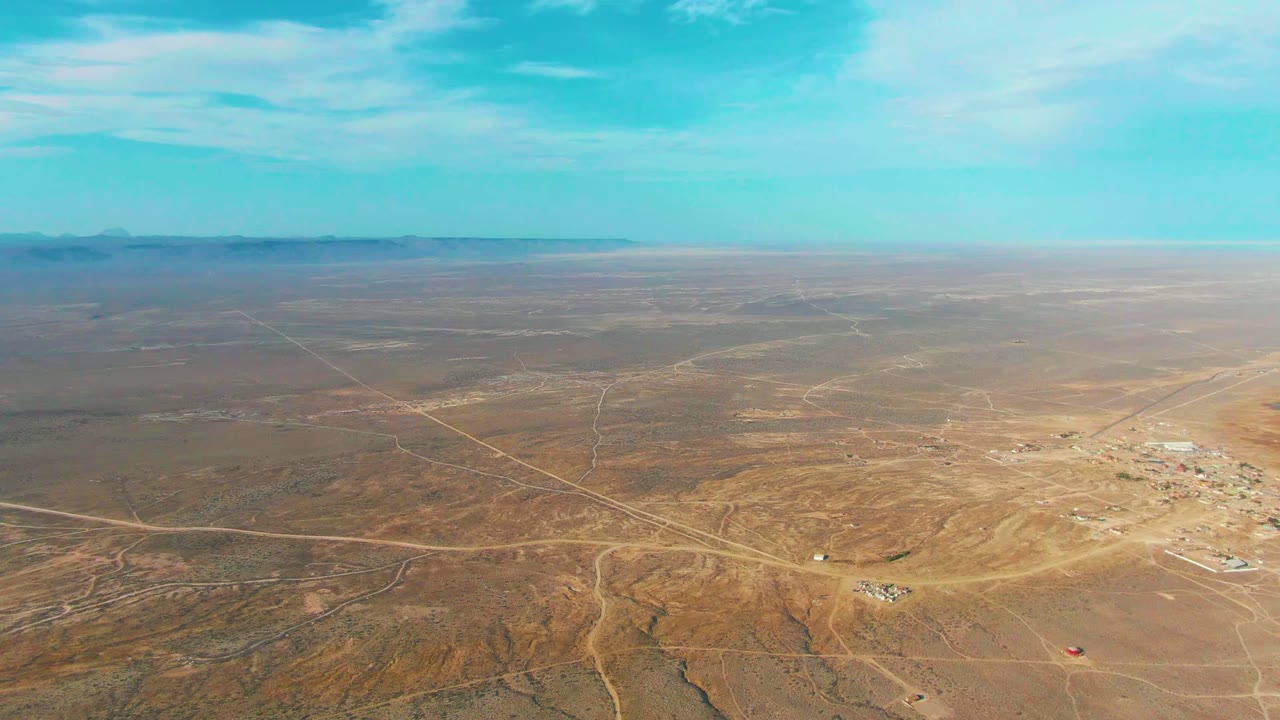 Aerial view of tan desert crossed by dirt tracks near sparse buildings