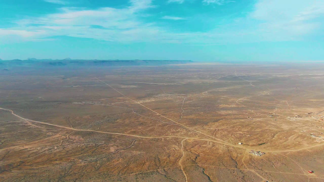 High desert aerial with dirt tracks crossing an open brown plain