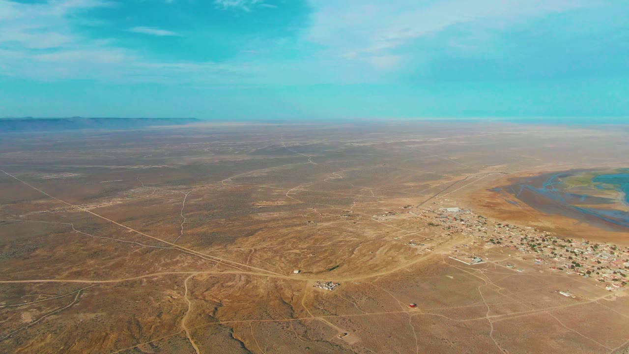High aerial view of desert tracks leading toward a small settlement and water.