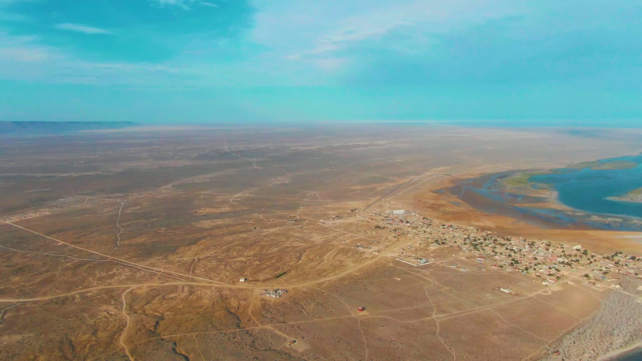 High aerial view of arid terrain, scattered structures, roads, and blue lagoon water