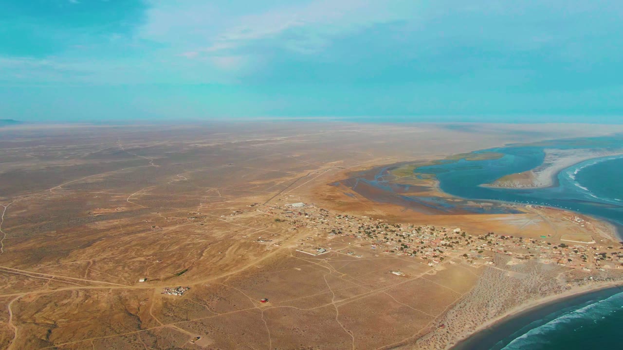 Desert village, sandbar, estuary water, and ocean edge seen from above.