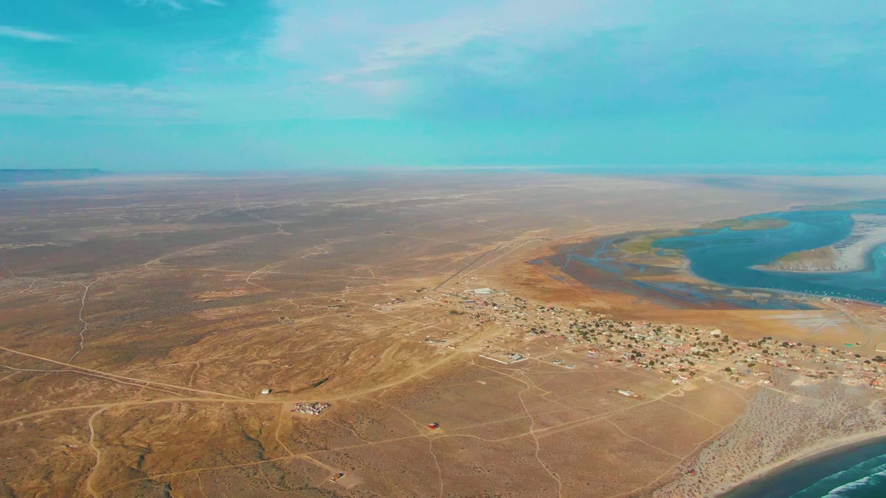 Aerial coastline with village grid, sandy terrain, and curved blue water