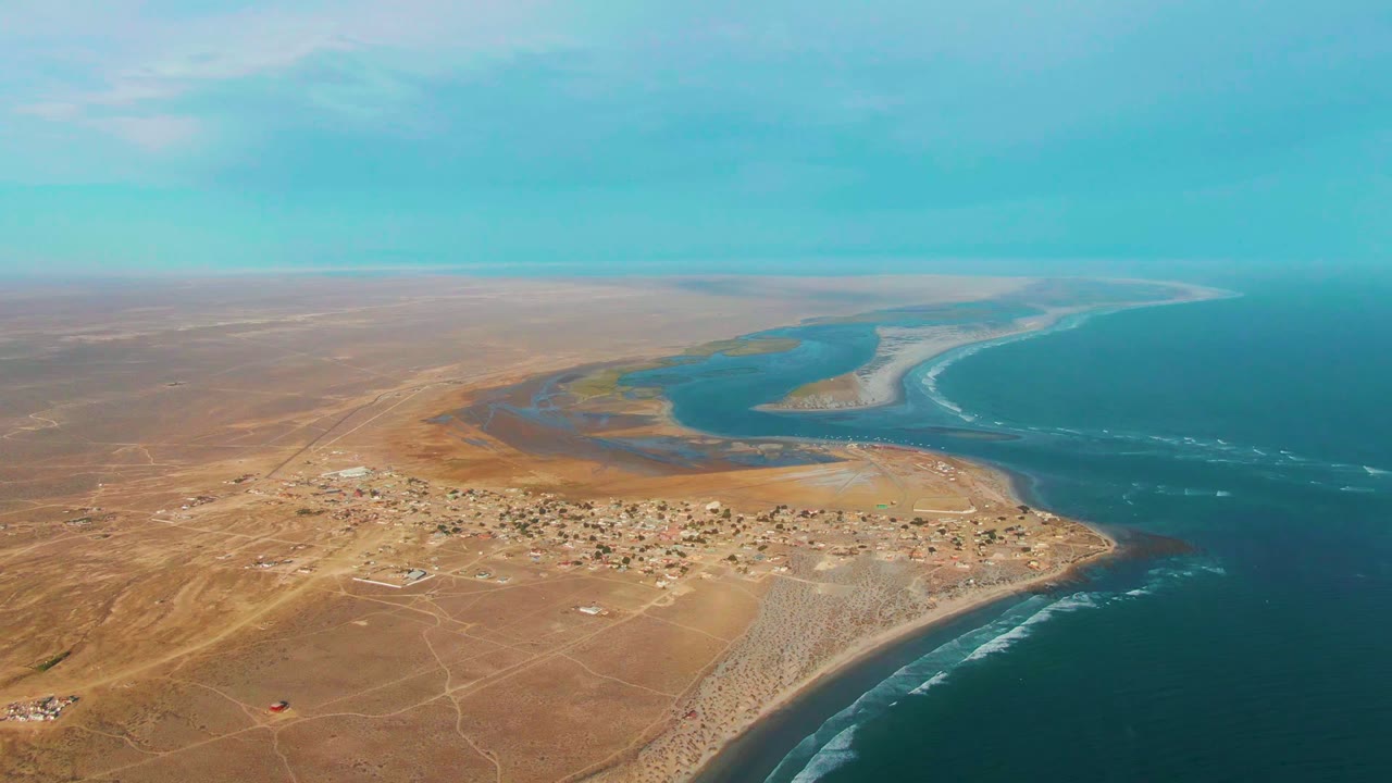 Desert settlement beside a lagoon and curving ocean shoreline.