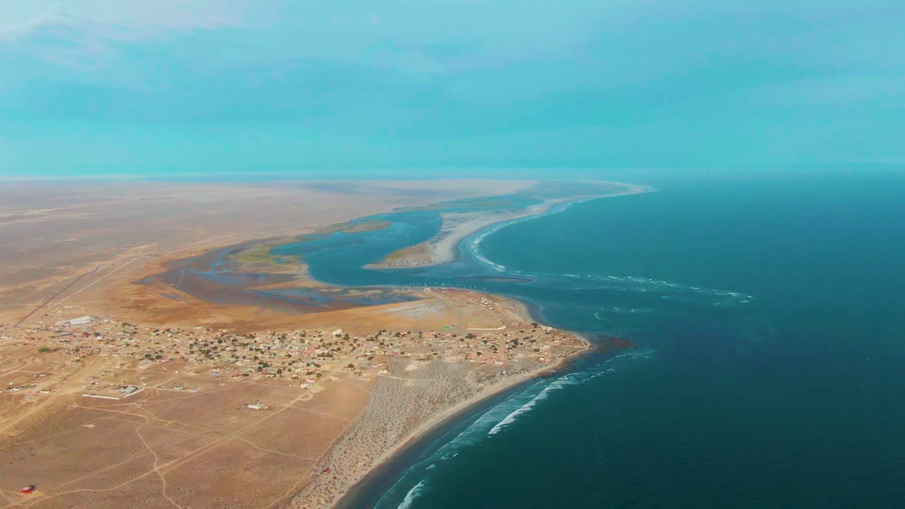 Wide aerial of a small coastal town beside lagoon water and open ocean.