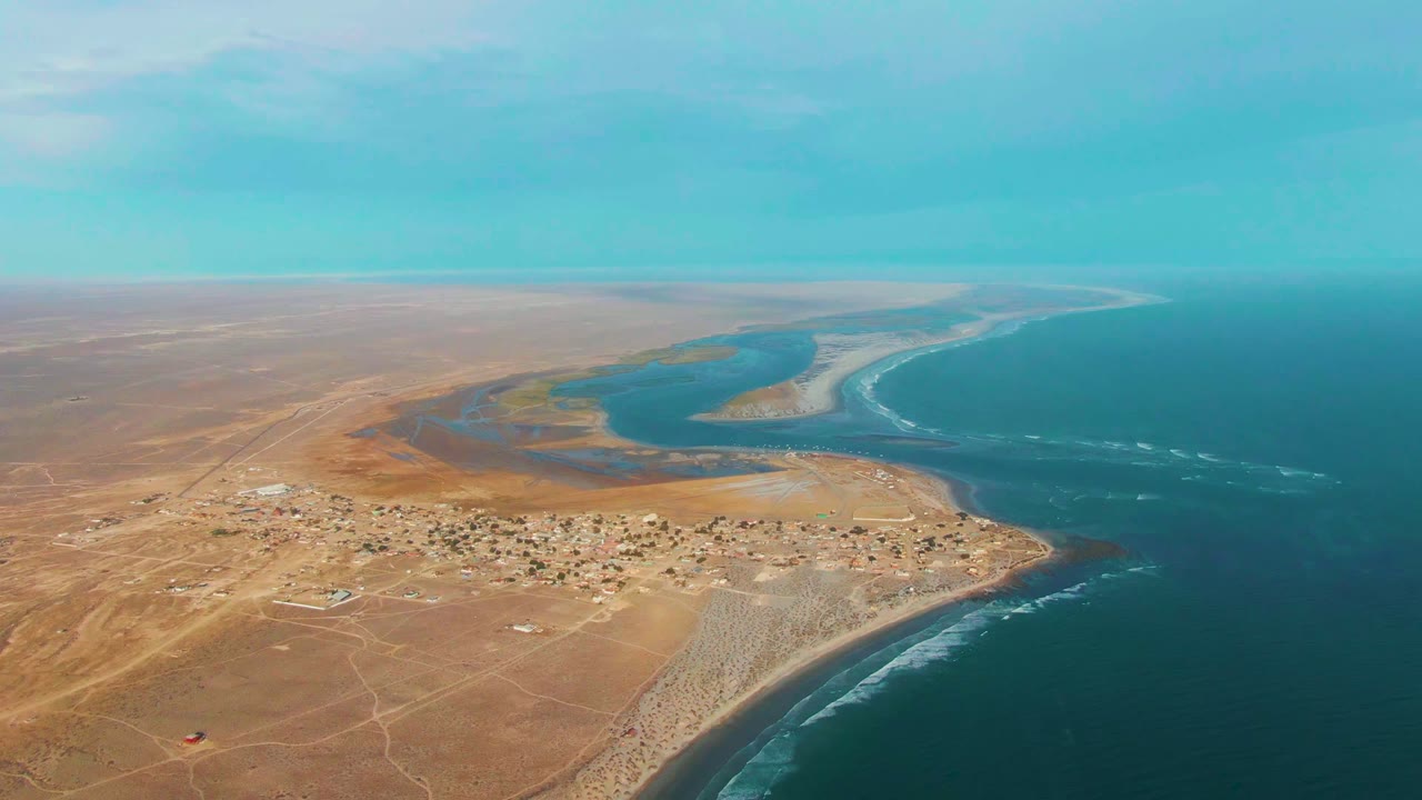 Wide aerial coastline with lagoon, settlement, sandbar, and ocean.