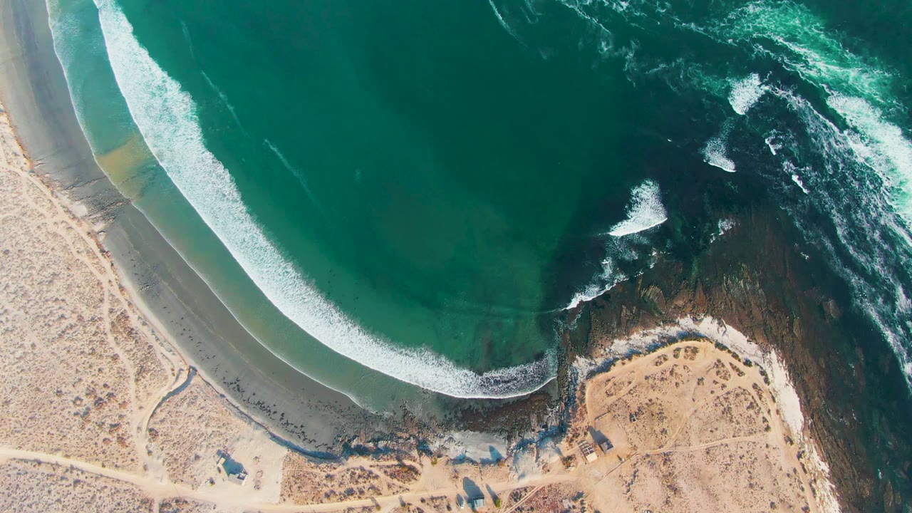 White wave line advancing toward a curved sandy beach