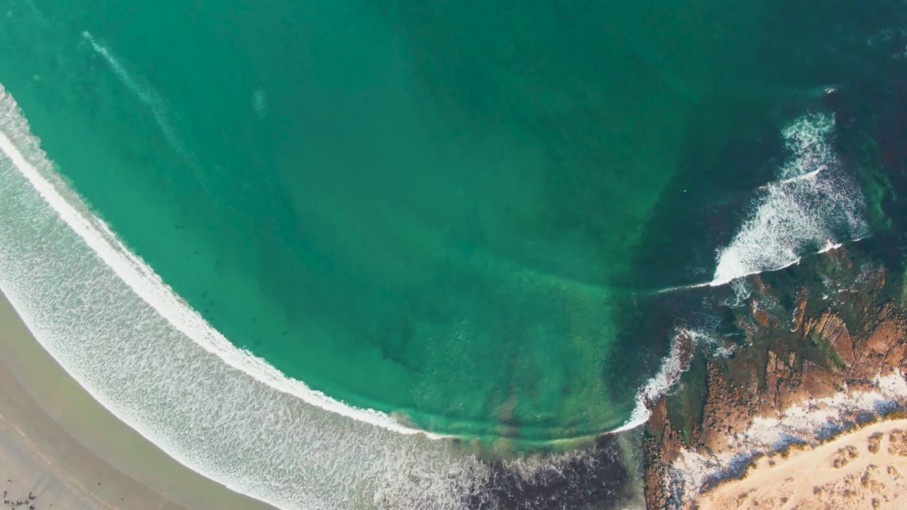 White wave arcs across clear water beside a rocky point